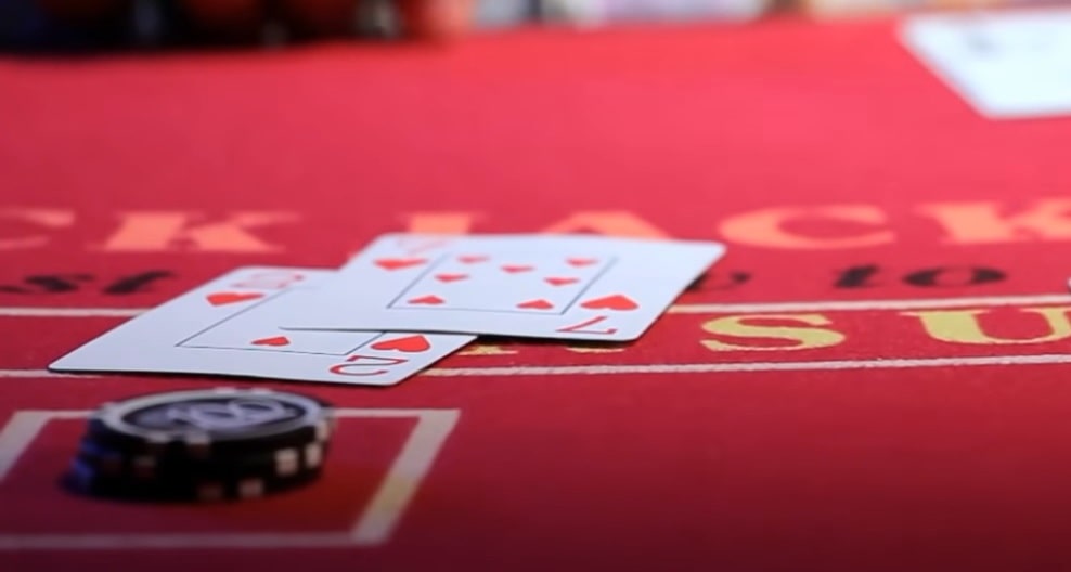 A poker player's face-down hole cards, two stacks of chips, and the dealer button on a  red felt table.